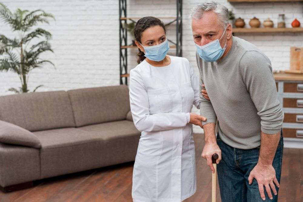 Elderly man using a cane receiving support from a caregiver while standing together in a home care setting