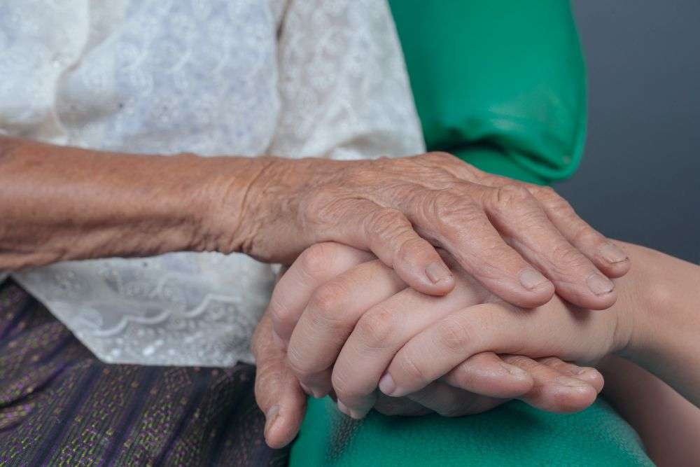 Elderly woman with Parkinson’s holding a caregiver’s hand for support and comfort at home