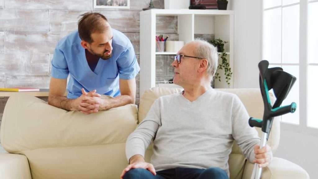 Caregiver talking with a senior using crutches.