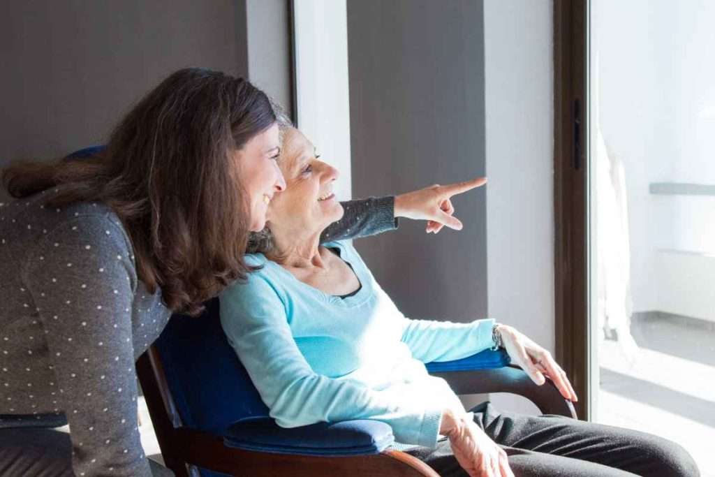 Caregiver and senior looking out a window together.